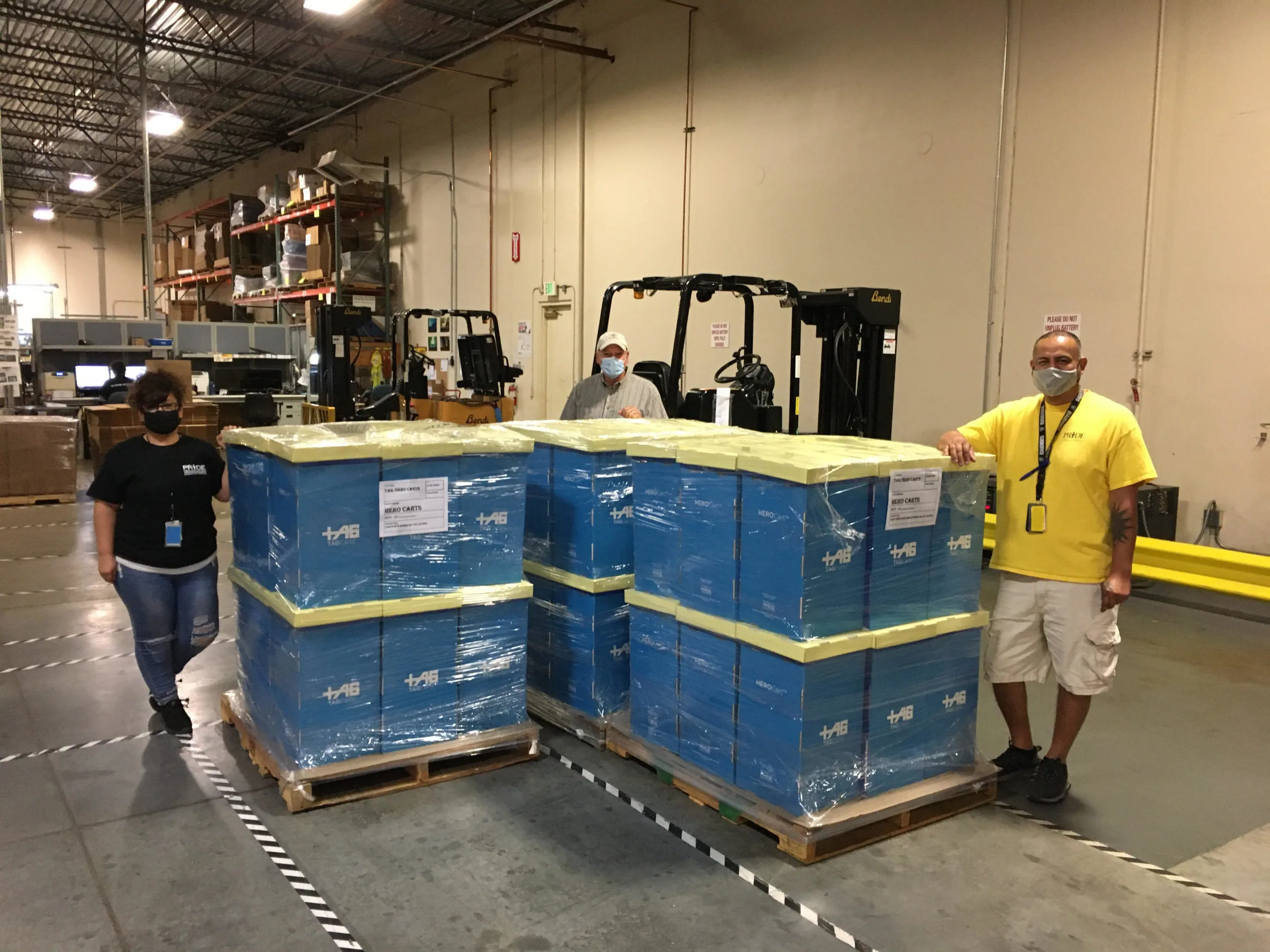 Three warehouse workers standing beside blue shipping crates stacked on pallets in industrial facility